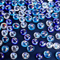 Flat iridescent blue glass marbles scattered on a dark blue surface, showing clear and deep blue colors with rainbow reflections.