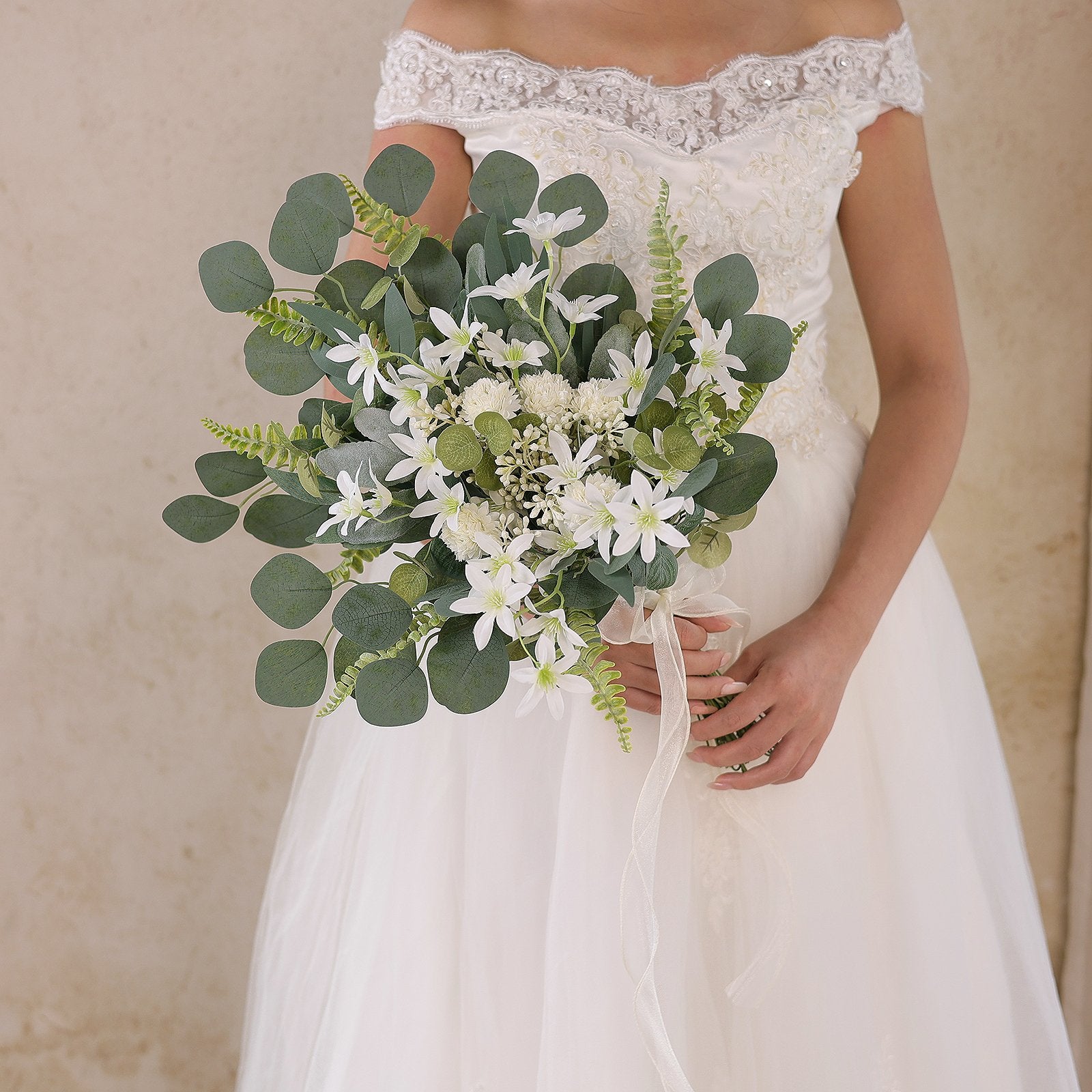 Bride in a white lace-trimmed wedding dress holding a bouquet of artificial greenery and white flowers.