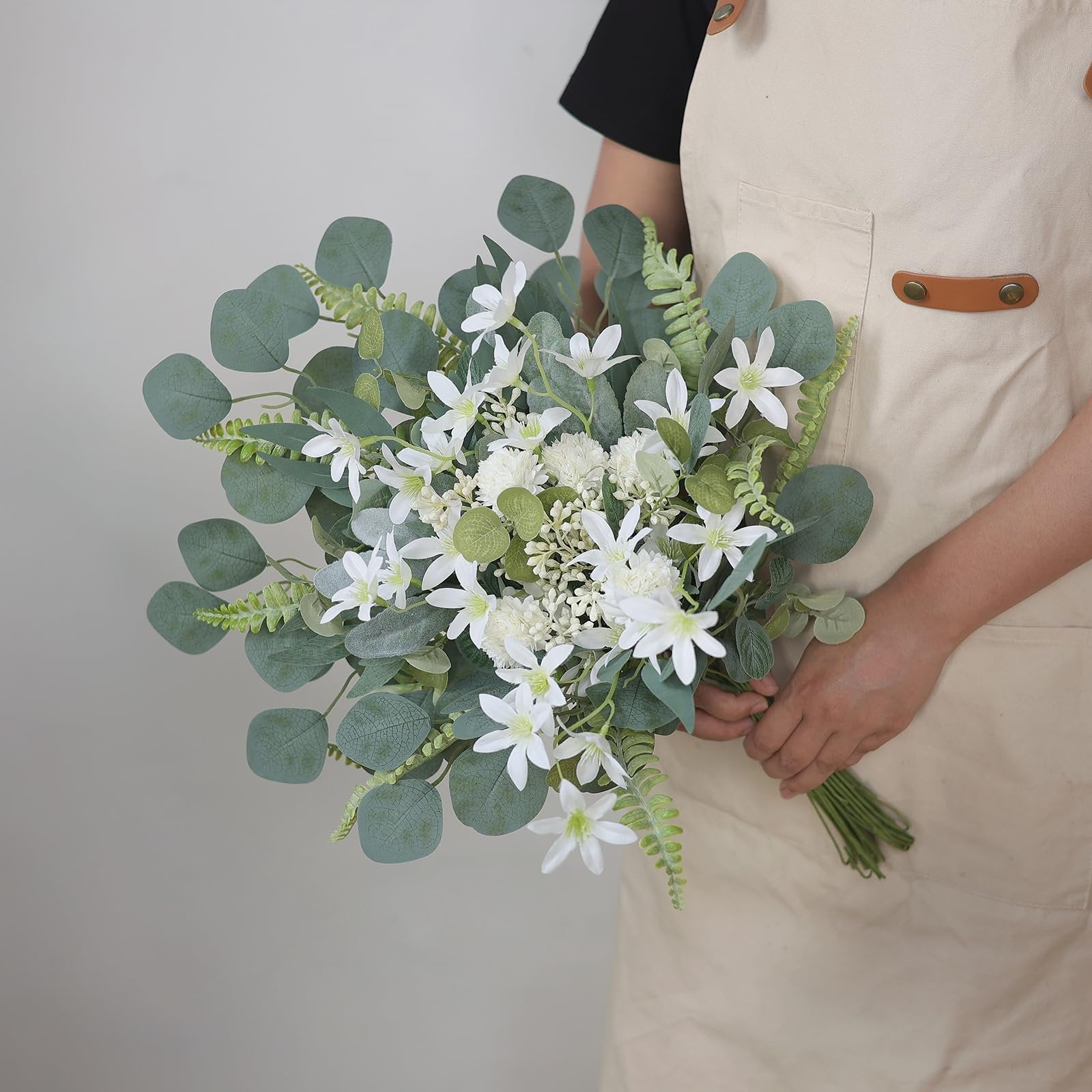 Person in apron holding a bouquet of artificial white flowers and green eucalyptus leaves