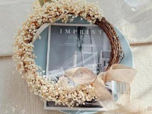 Dried baby's breath wreath with a beige bow resting on a blue plate over a magazine.
