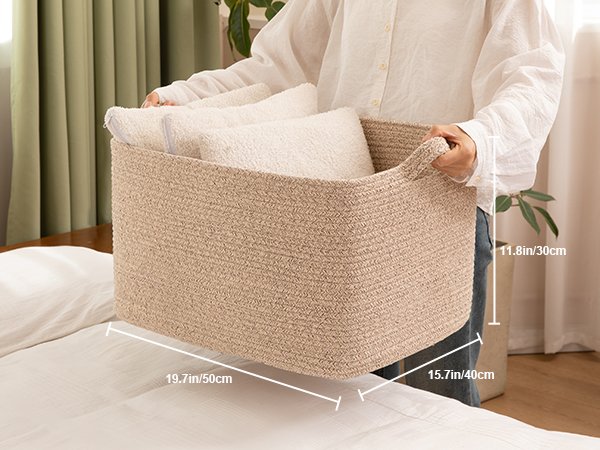 Person holding a large beige woven rope basket filled with white towels, showing dimensions.