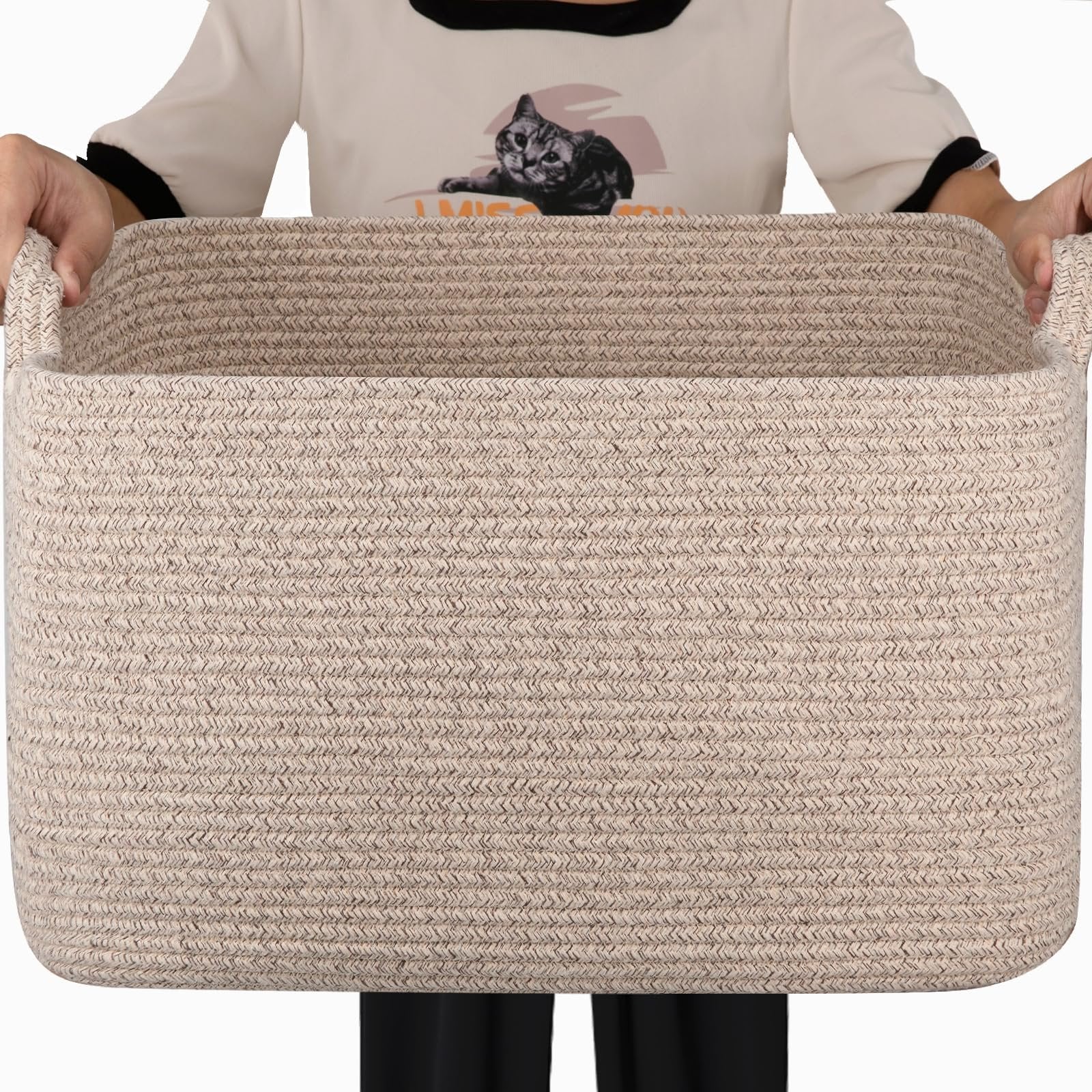 Person holding a large beige woven cotton rope storage basket with handles, front view.