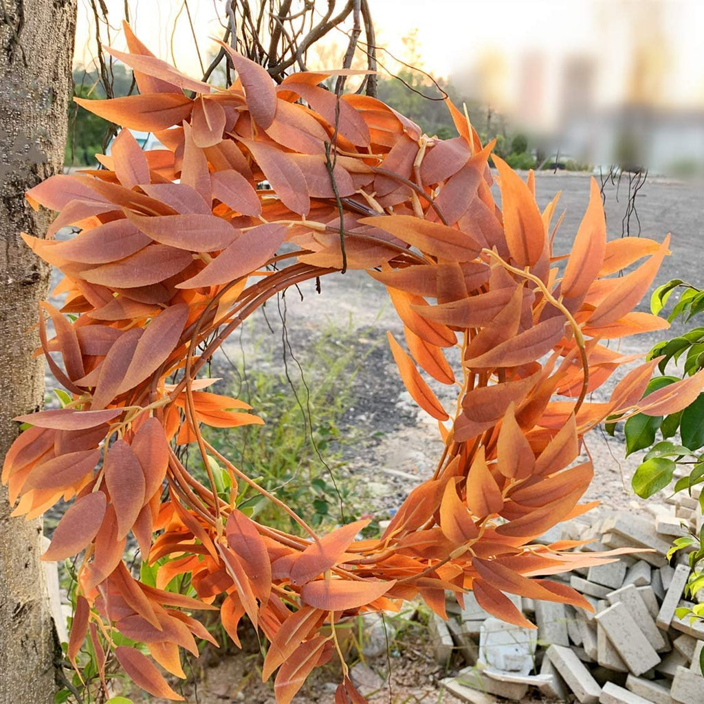 Artificial orange leaf garland wreath hanging on a tree trunk outdoors with blurred background