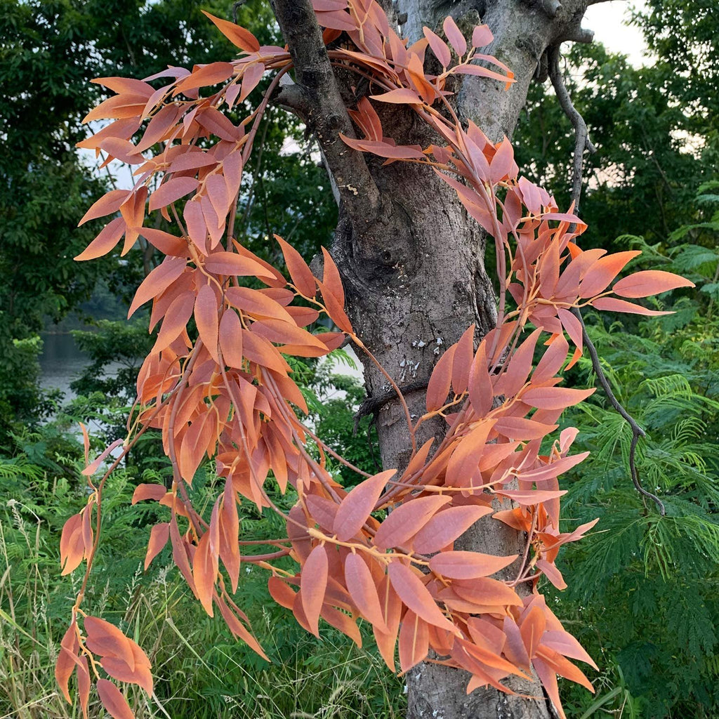 Artificial silk leaf garland with copper-toned leaves wrapped around a tree trunk outdoors.