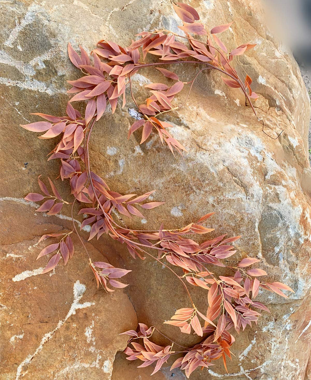 Artificial silk leaf garland with reddish-brown leaves draped over a textured rock surface.