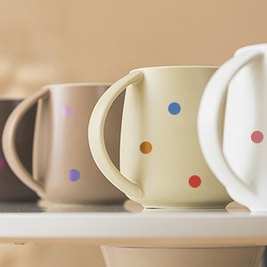 Four ceramic mugs in various neutral colors, each decorated with colorful dot stickers in a repeating pattern.