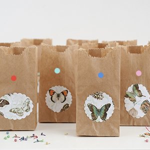 Several brown paper bags decorated with butterfly stickers and colorful dot stickers, arranged in a row.