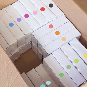 Cardboard box filled with white packages, each with a colored dot sticker on top.