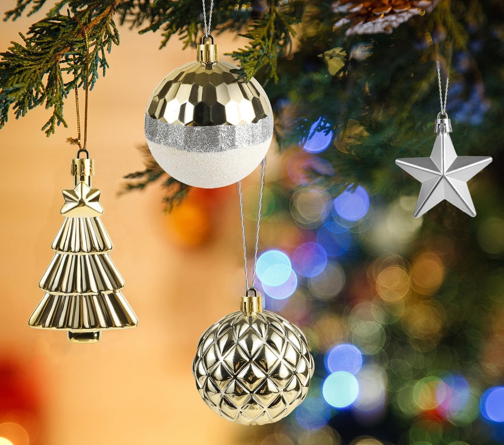 Assorted white and gold Christmas ornaments including a tree, baubles, and a star, hanging on a tree branch with bokeh lights in the background.