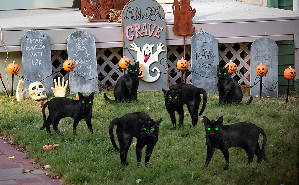 Six black cat Halloween yard signs with glowing green eyes arranged on a lawn with tombstones and pumpkins.