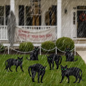 Six black cat silhouettes with green eyes on a lawn in front of a house with a banner and decorations, in the rain.