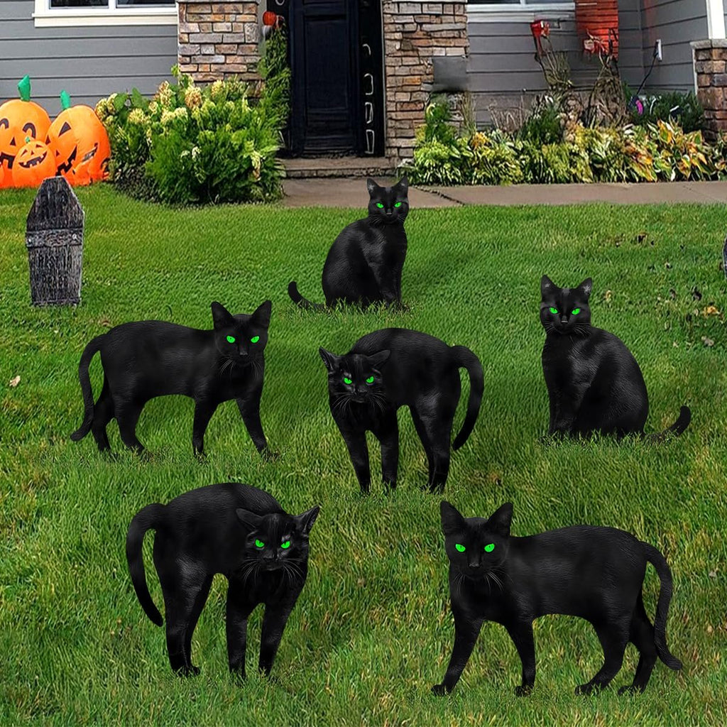 Six black cat silhouette yard signs with glowing green eyes arranged on a lawn in front of a house with Halloween decorations.
