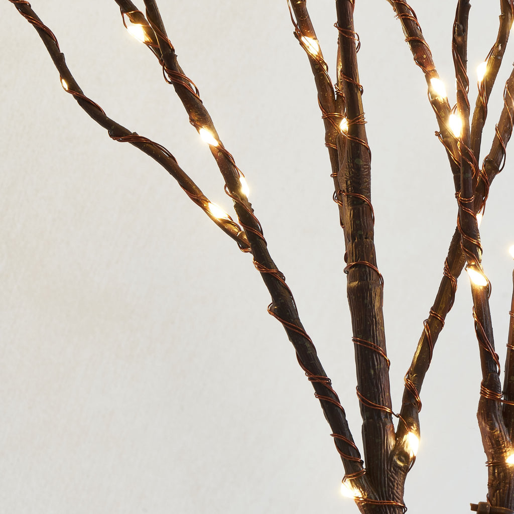 Close-up of brown twig branches with copper wire and fairy lights against a light background.