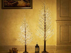 Two illuminated brown twig trees with fairy lights, one tall and one short, displayed indoors with a lantern and decorative reindeer.