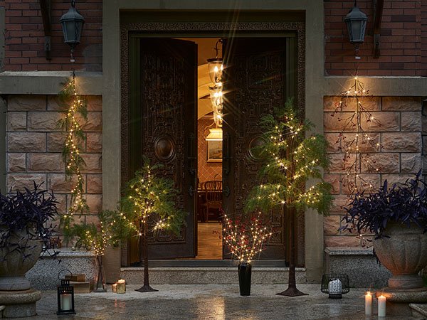 Brown twig garlands with fairy lights decorating trees and building exterior at dusk