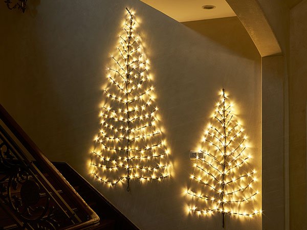 Two brown twig garlands shaped like Christmas trees with 120 warm white fairy lights, mounted on a wall next to a staircase.