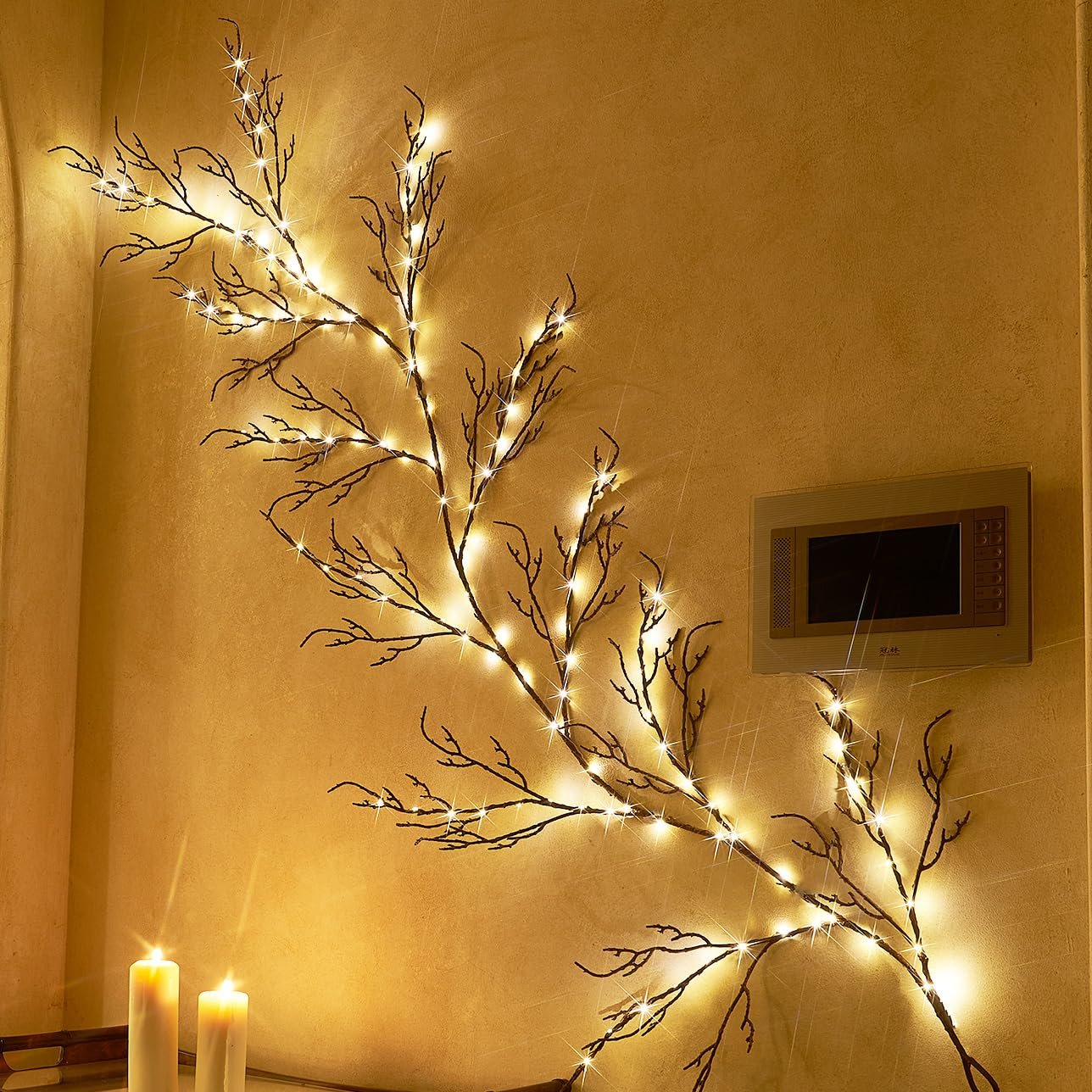 Brown twig garland with 120 fairy lights draped on a wall next to two lit candles and a wall-mounted intercom.