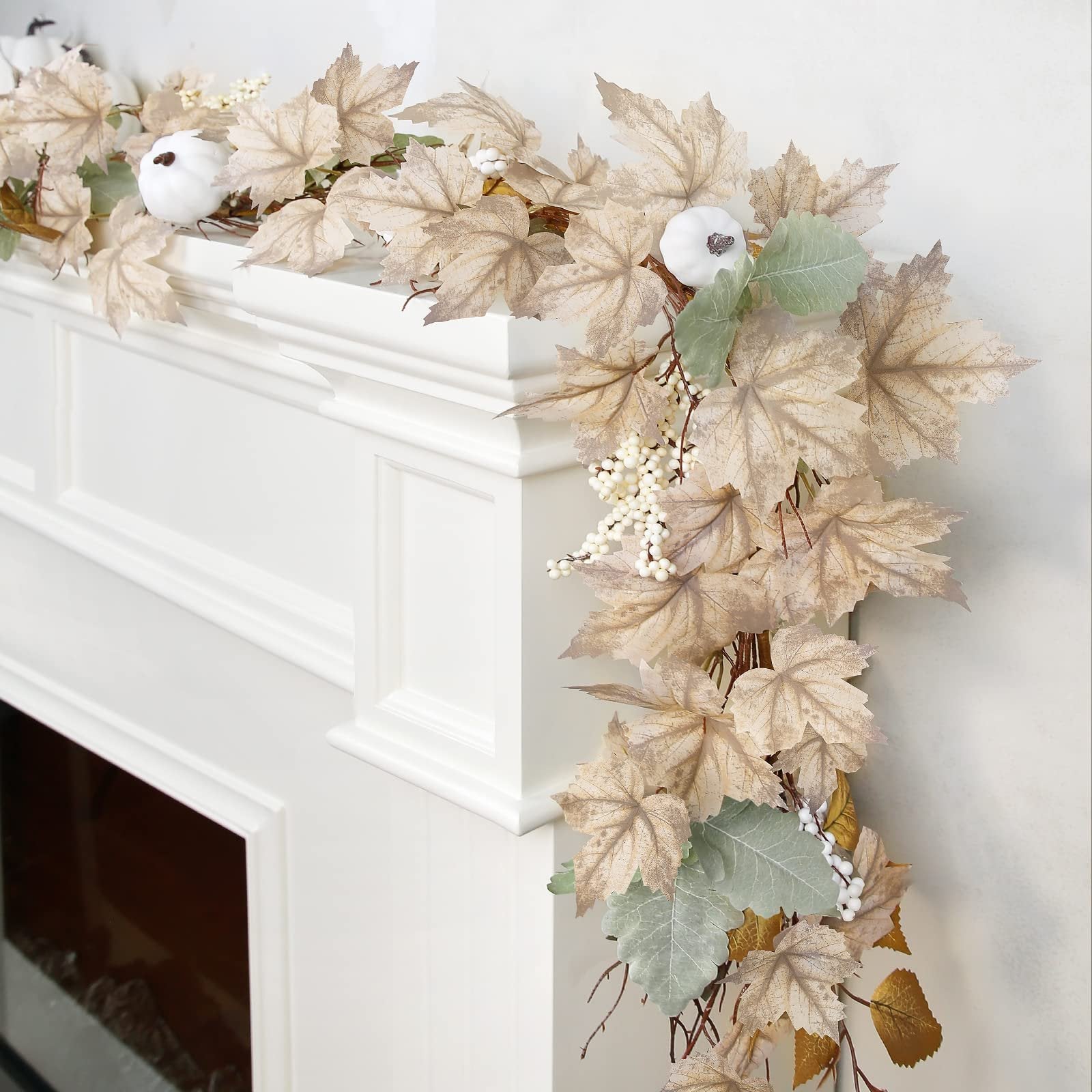 Autumn garland with maple leaves, pumpkins, and berries draped over a white fireplace mantle.