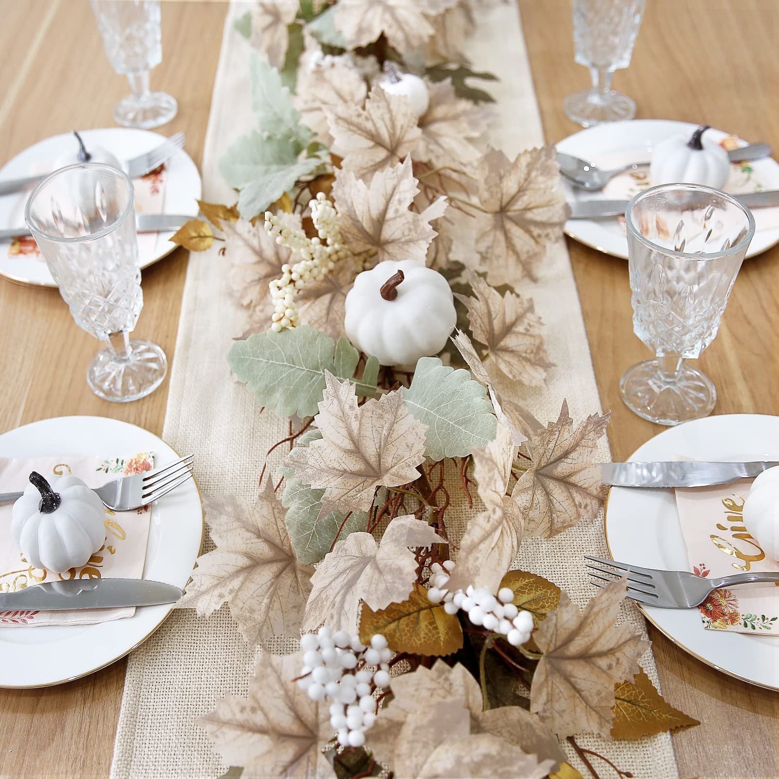Autumn garland with maple leaves, pumpkins, and berries on a table setting with plates, glasses, and cutlery.