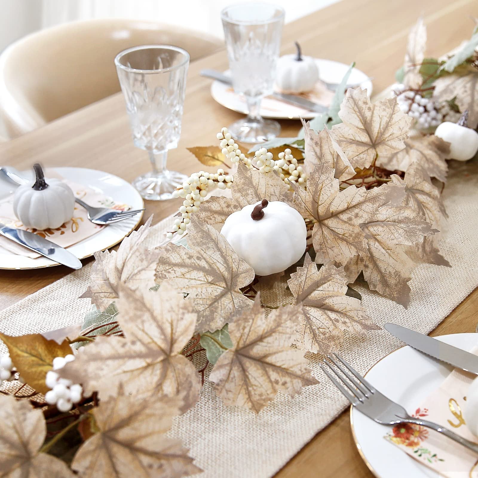Autumn garland with maple leaves, pumpkins, and berries arranged on a table setting with plates and glasses.