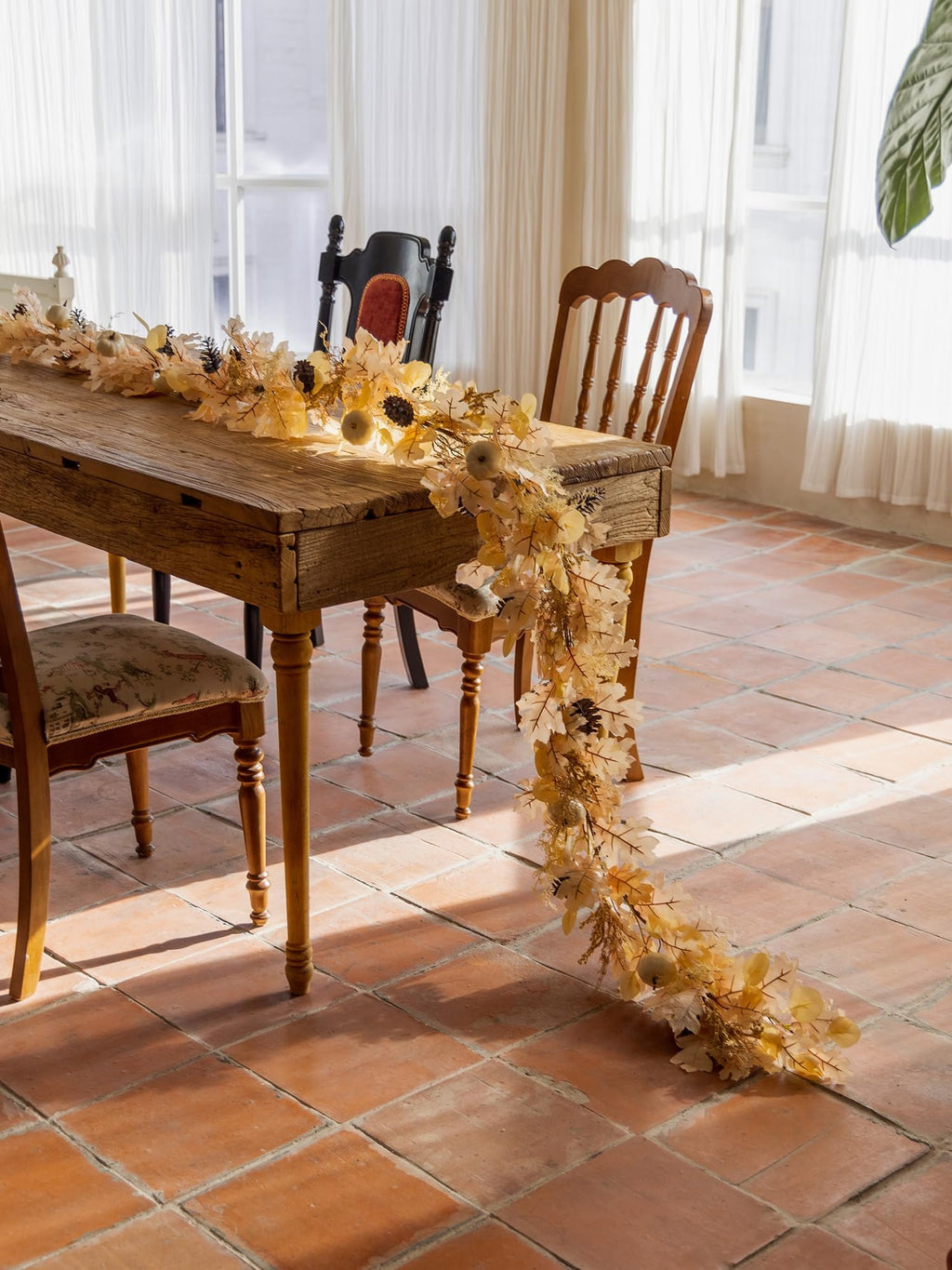 Boho fall garland with artificial pumpkins, berries, and maple leaves draped across a rustic wooden table.