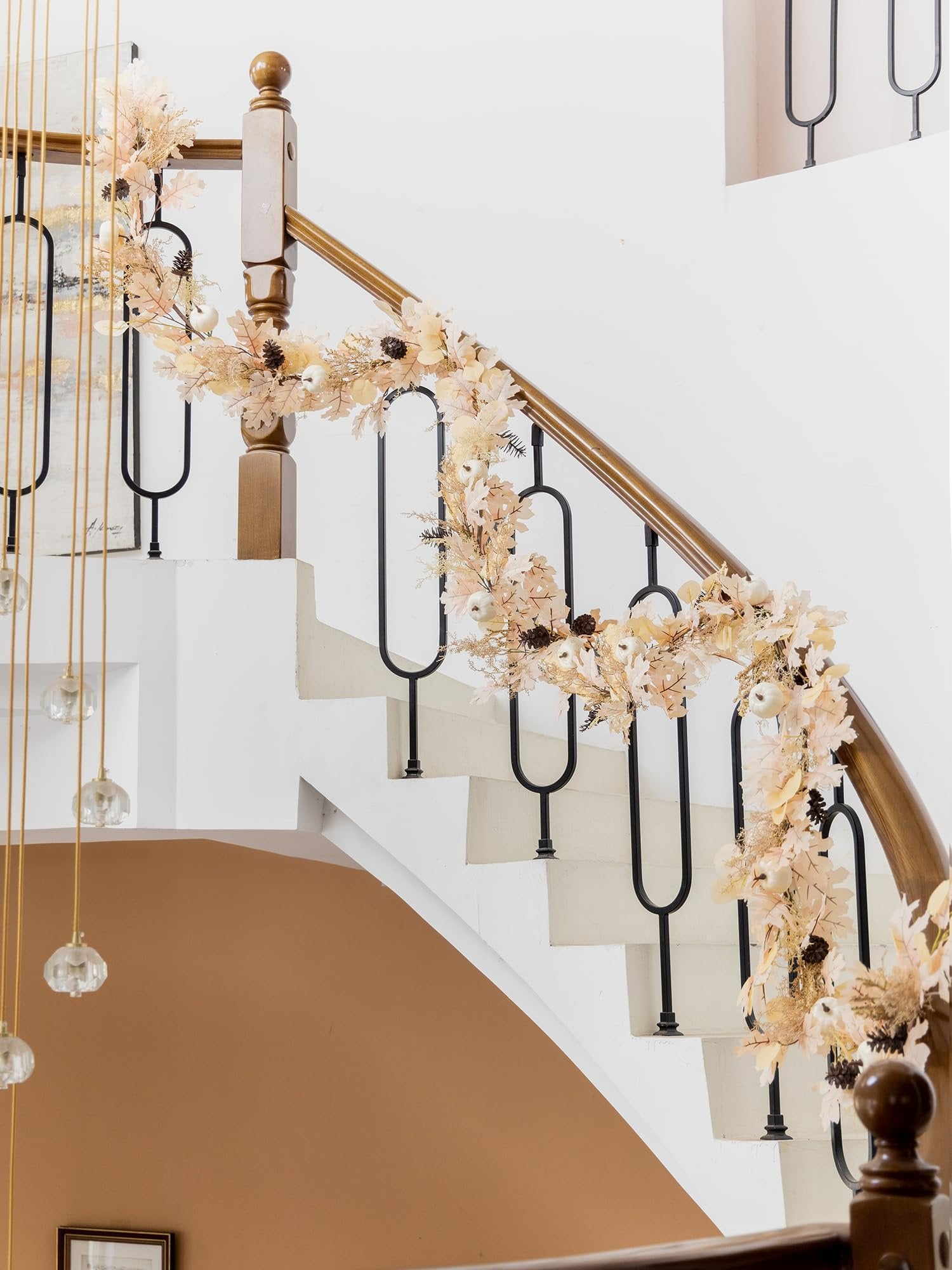 Boho fall garland with artificial leaves, pumpkins, and pinecones draped on a staircase railing.