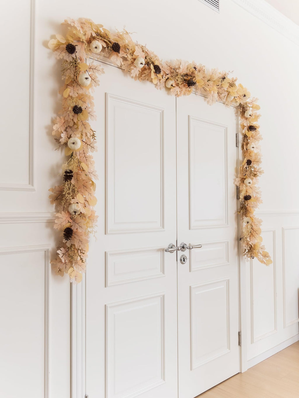 Boho fall garland with artificial leaves, white pumpkins, and pinecones draped over a white double door.