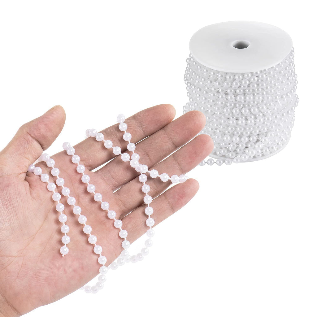 Hand holding a strand of white faux pearl garland with a spool of the same garland in the background.