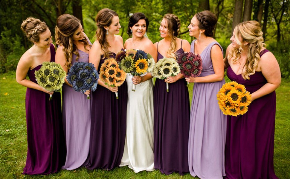 Wedding party holding bouquets of artificial sunflowers in various colors, standing outdoors.