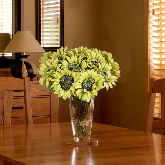 Bouquet of light green silk sunflowers in a clear glass vase on a wooden table.