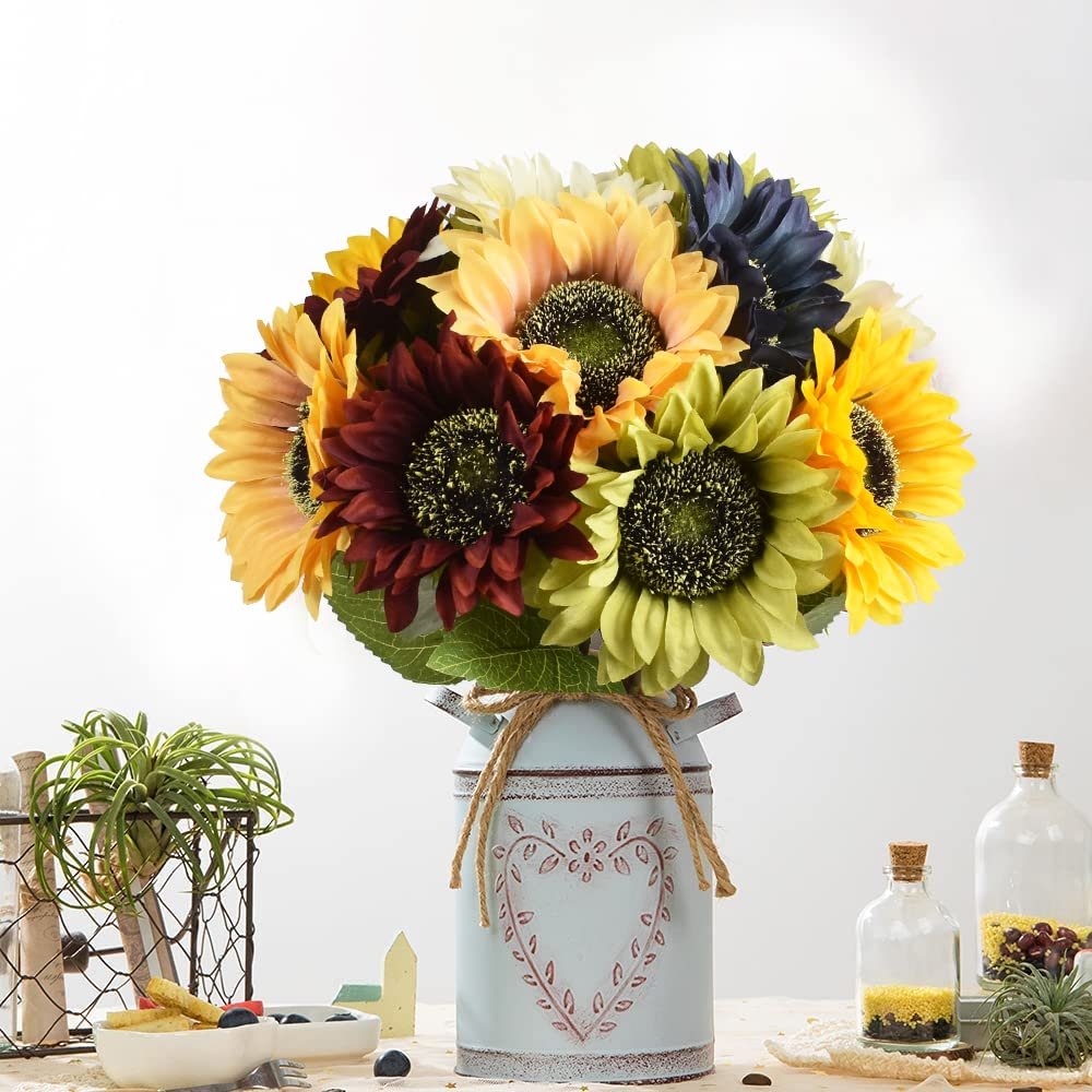 Bouquet of assorted silk sunflowers in a decorative metal vase with a heart design, set on a table with other decor items.