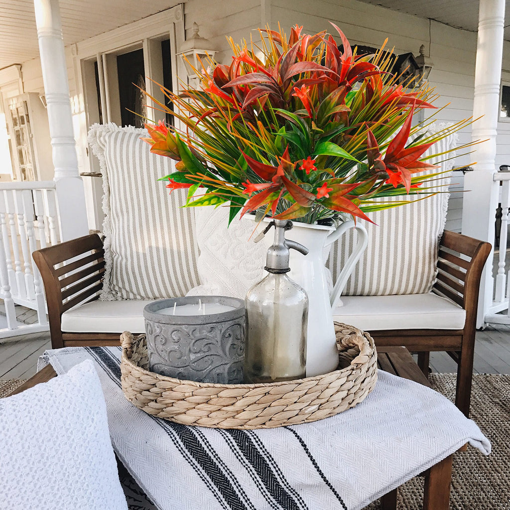 Artificial orange and red morning glory flowers in a white pitcher on a porch bench