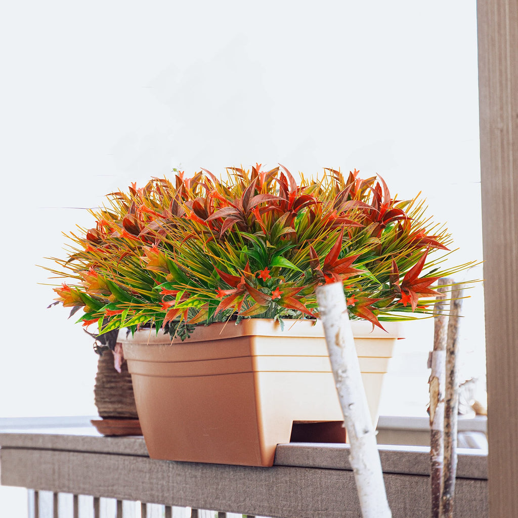 Artificial morning glory flowers and orange grass in a tan planter on a railing