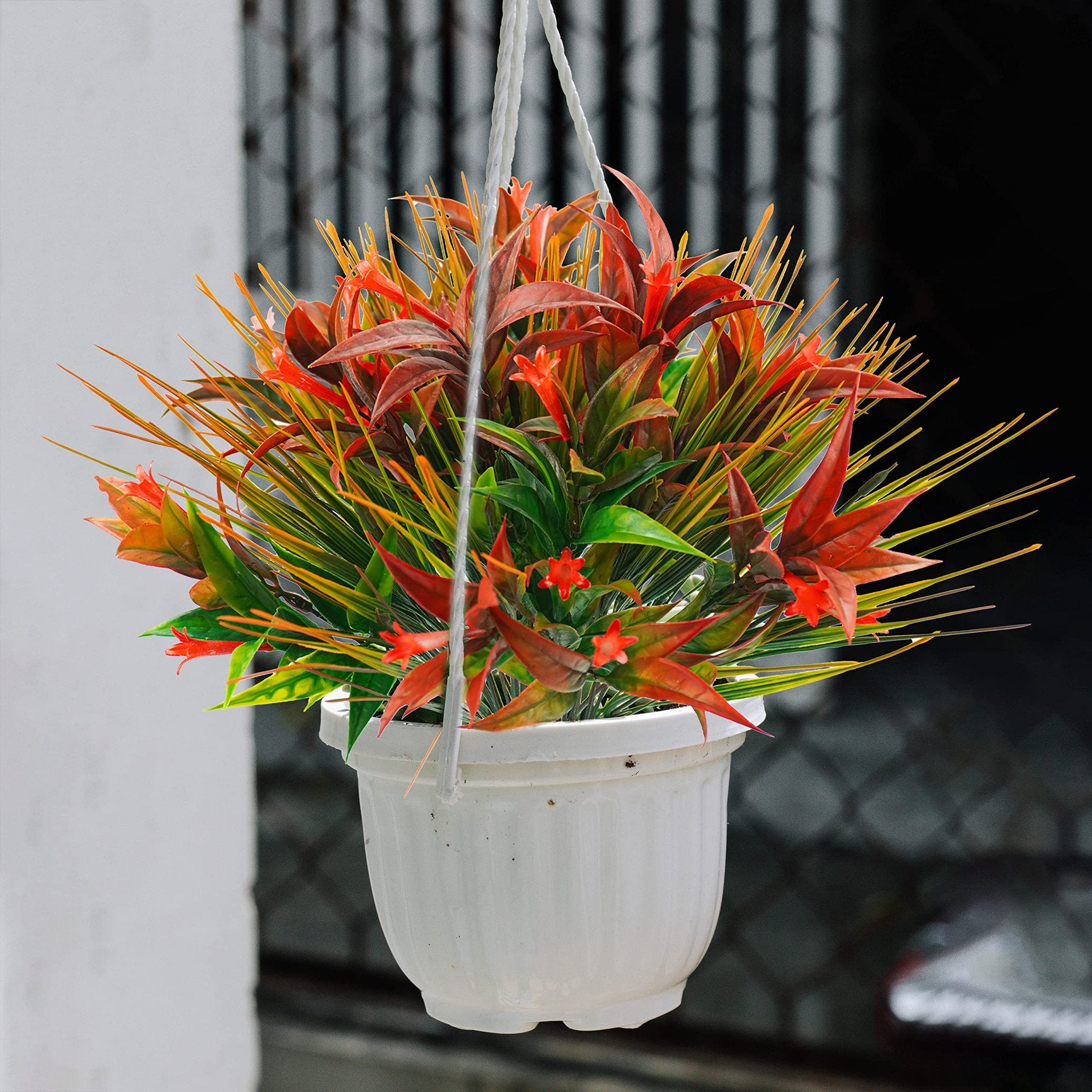 Hanging artificial plant with red and orange flowers and green foliage in a white pot.