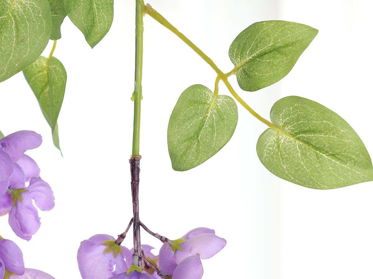 Close-up of artificial purple wisteria flowers and green leaves on a white background.