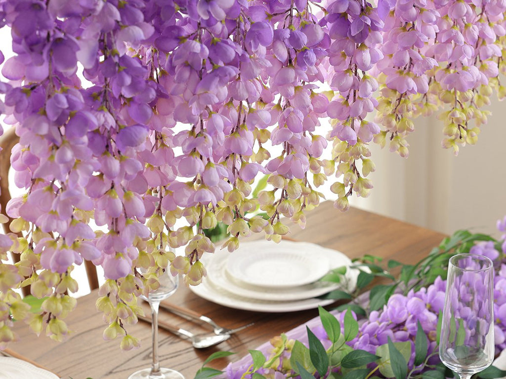 Purple wisteria hanging flowers draped over a wooden table with place settings and a wine glass.