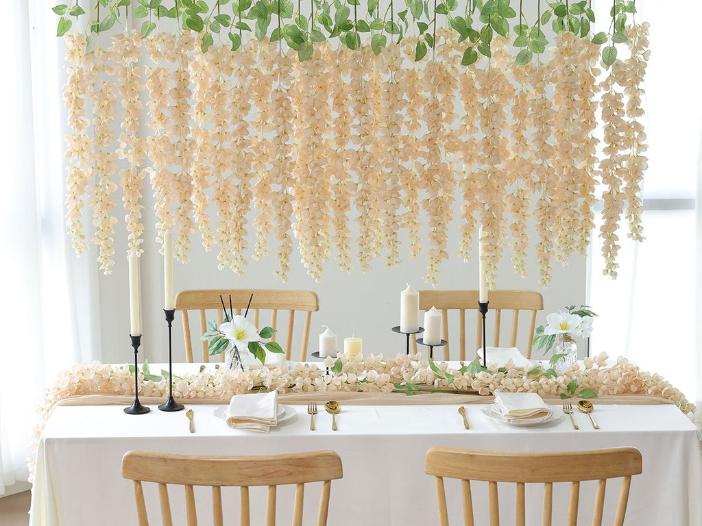 Table setting with hanging peach wisteria flowers and greenery, candles, and place settings.