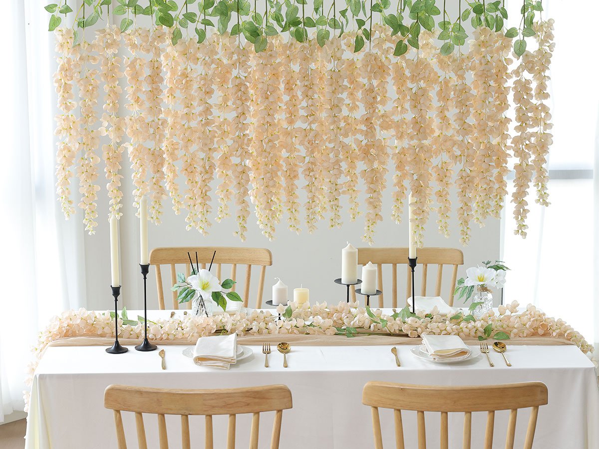 Table setting with hanging peach wisteria flowers and greenery, candles, and place settings.