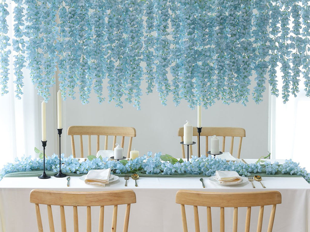 Table setting with blue wisteria flowers draped overhead and along the table runner, featuring candles and place settings.