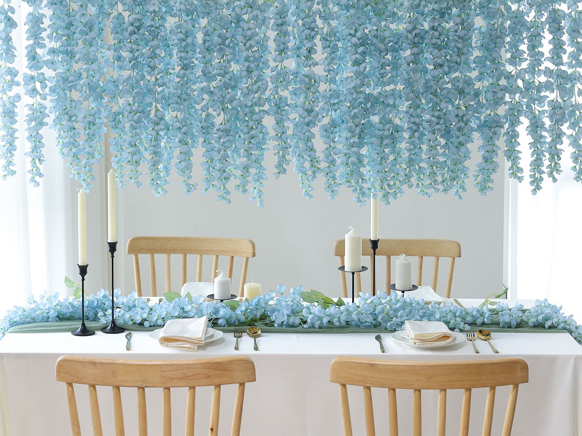 Table setting with blue wisteria flowers draped overhead and along the table runner, featuring candles and place settings.