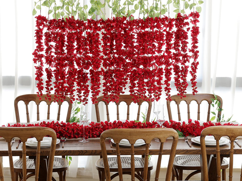Red wisteria hanging flowers and garland draped over a wooden dining table set for a meal.