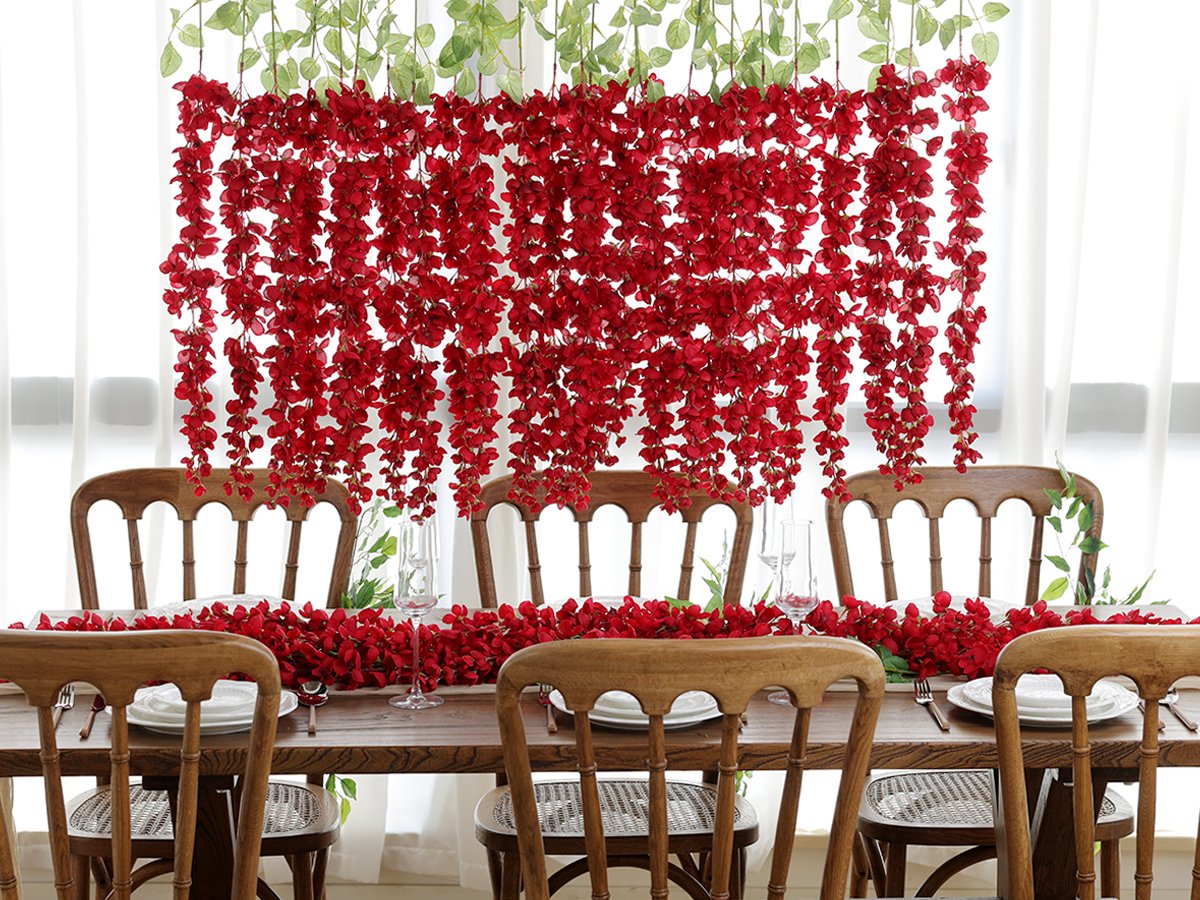 Red wisteria hanging flowers and garland draped over a wooden dining table set for a meal.