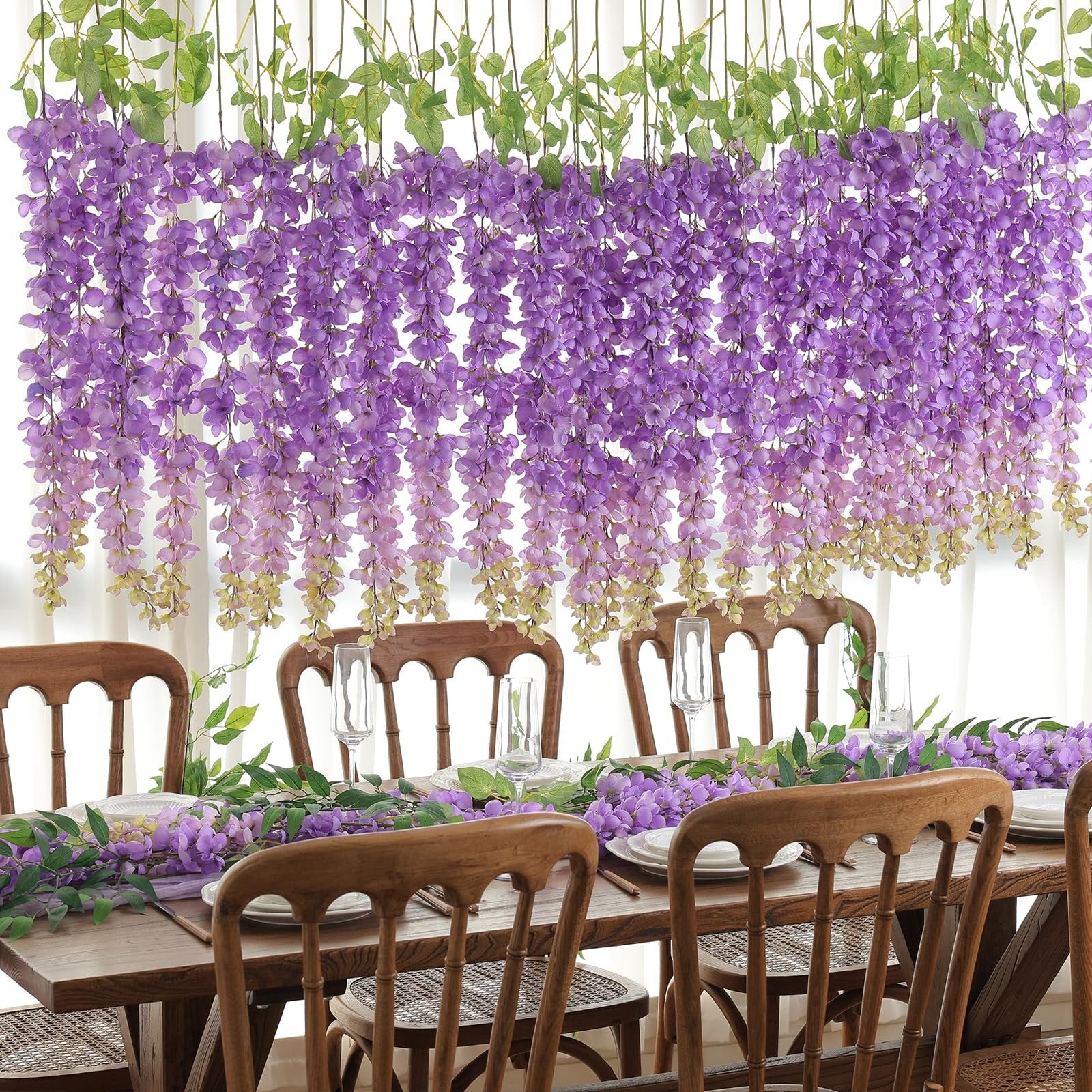 Purple wisteria hanging flowers and garland draped over a wooden dining table set for a meal.