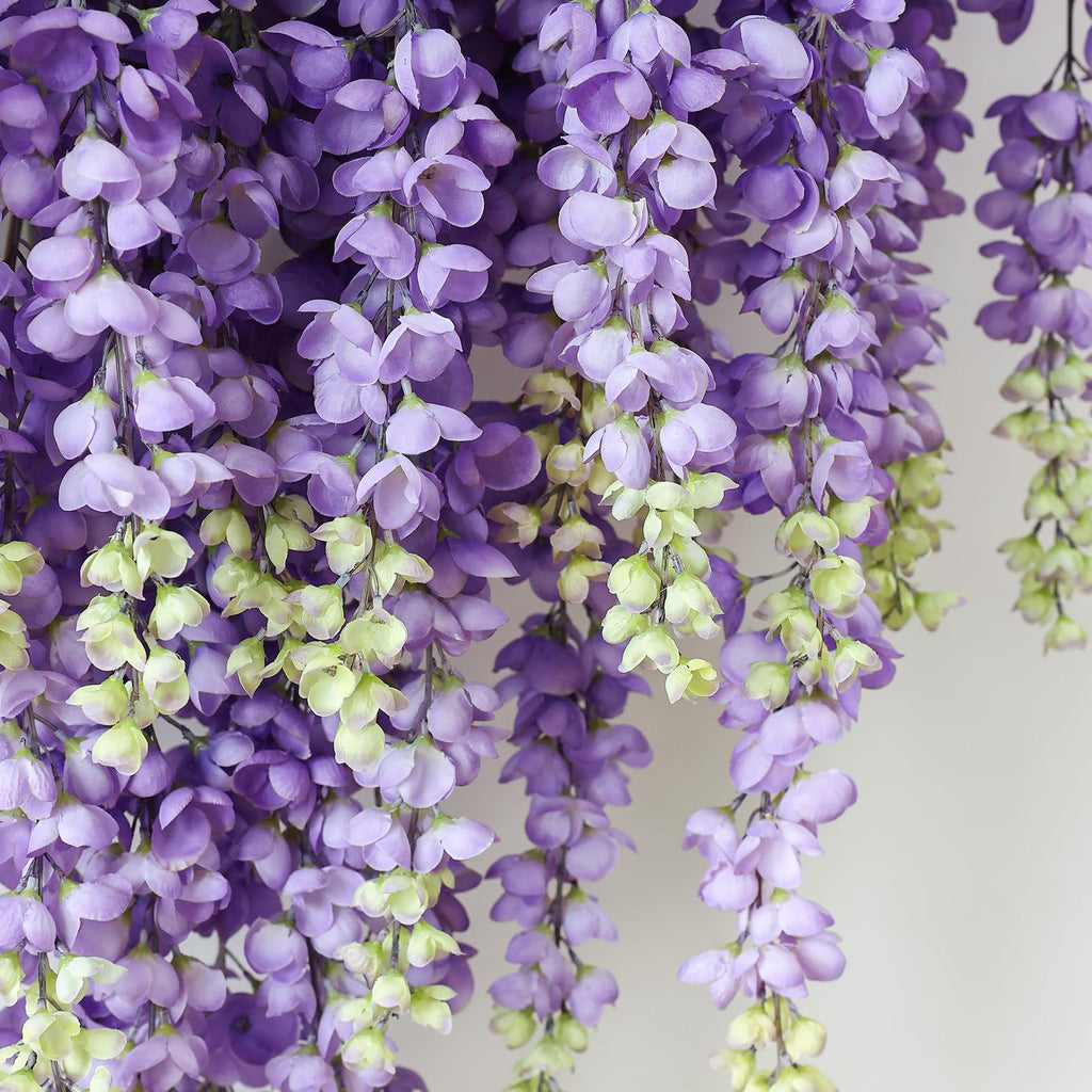 Close-up of cascading purple wisteria artificial flowers against a light background.