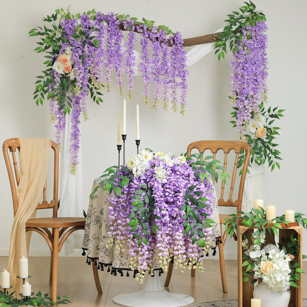 Wedding arch decorated with purple wisteria garlands and white fabric, with a table set for two.