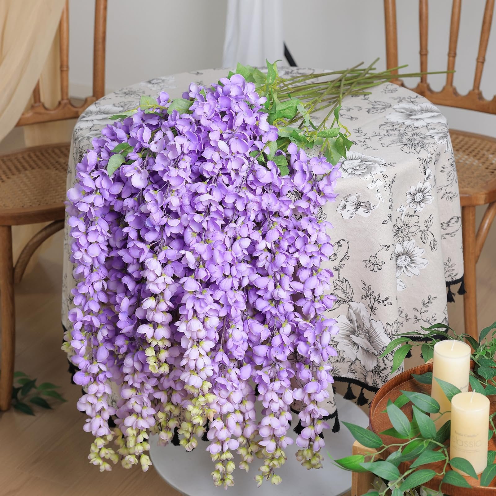 Purple wisteria hanging flowers draped over a table with two chairs and candles in the foreground.