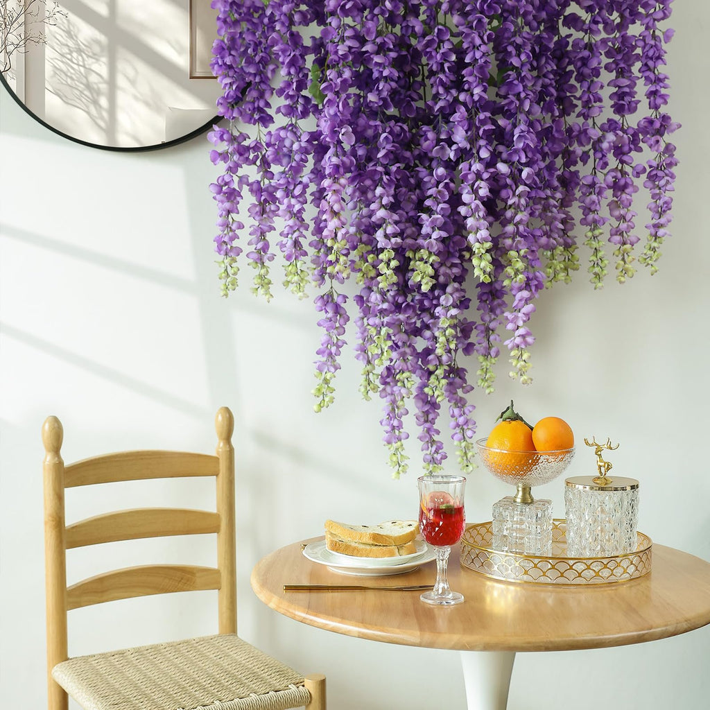 Purple wisteria hanging flowers draped over a table with a chair, fruit bowl, and drink.
