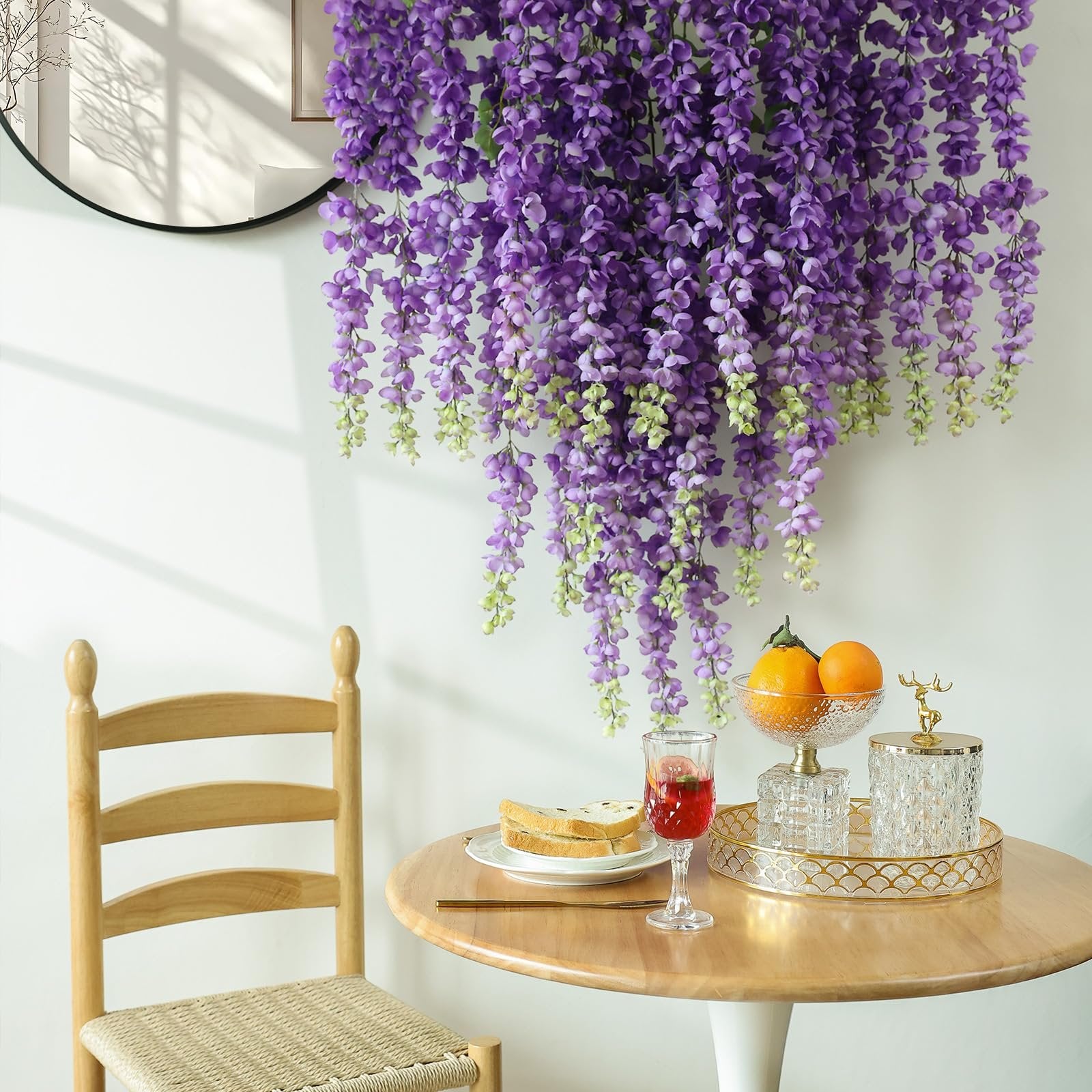 Purple wisteria hanging flowers draped over a table with a chair, fruit bowl, and drink.