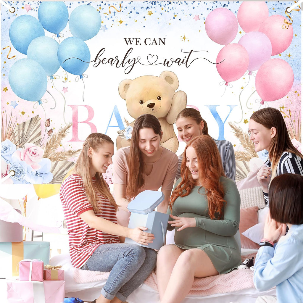 Group of women at a gender reveal party opening a gift, with a boho bear backdrop.