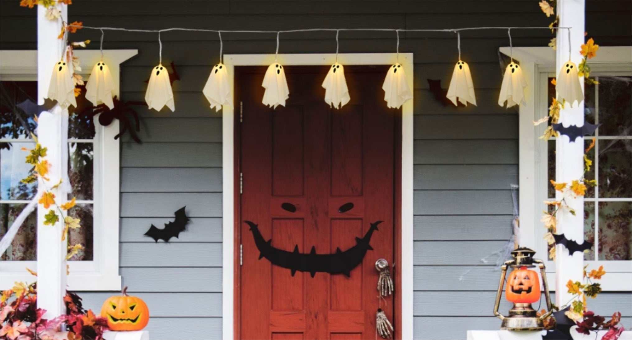 Halloween porch decorated with ghost string lights, bats, pumpkins, and a jack-o-lantern lantern.